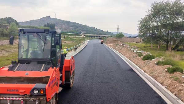 6月18日，由西部市政建设集团承建的东乡县那勒寺镇沿川经济带产业道路施工现场机械轰鸣，沥青摊铺机缓缓向前推进，滚烫的沥青混合料均匀摊铺在水稳层上，压路机紧随其后反复碾压，一条黝黑发亮的“黑色丝带”向远